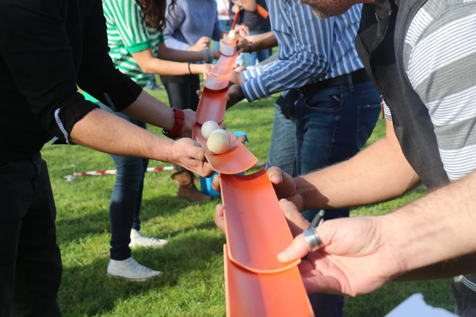 Team guiding a ball along linked orange channels during an outdoor team-building game on grass