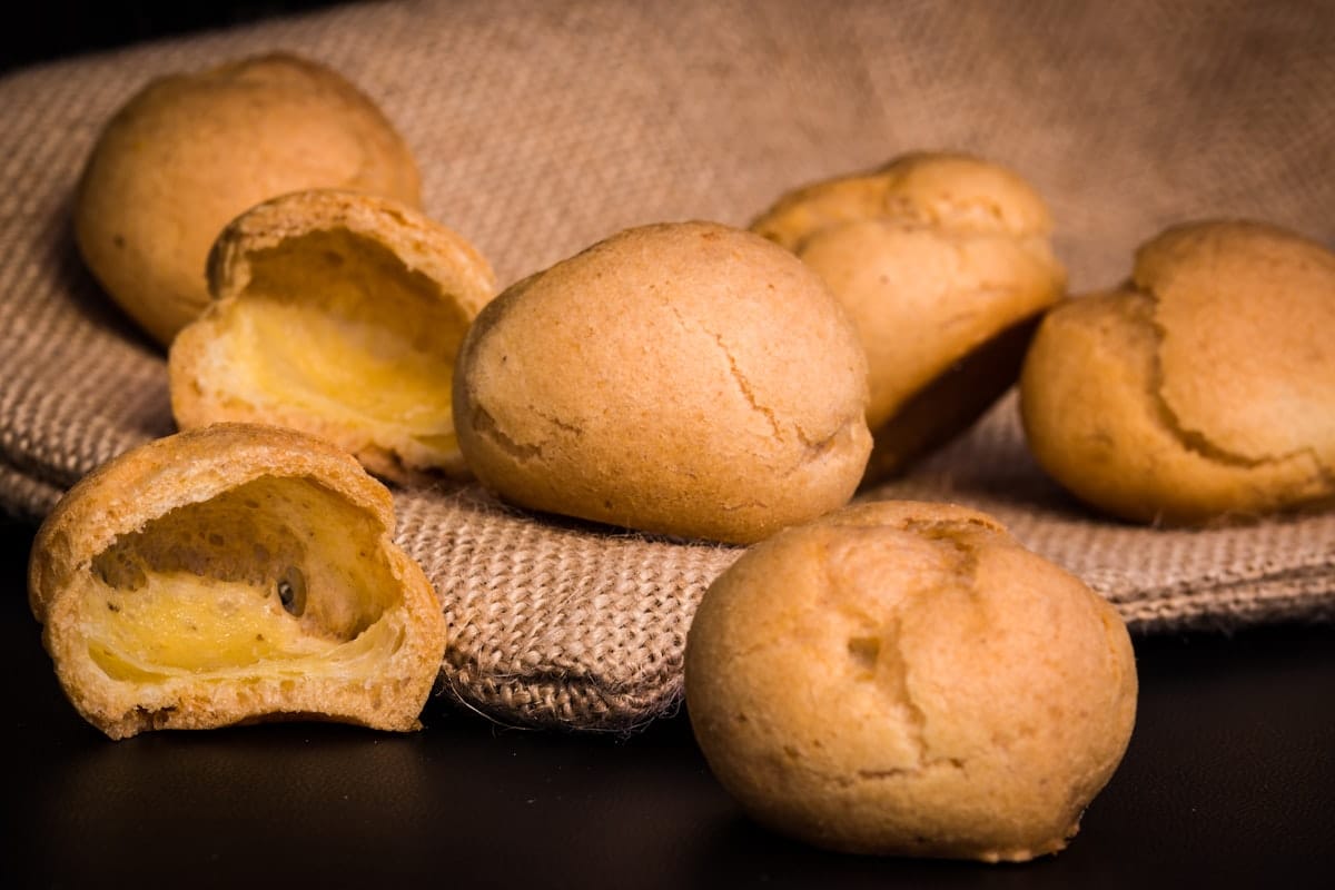 Golden pão de queijo cheese breads on burlap, two split open to show the soft centre