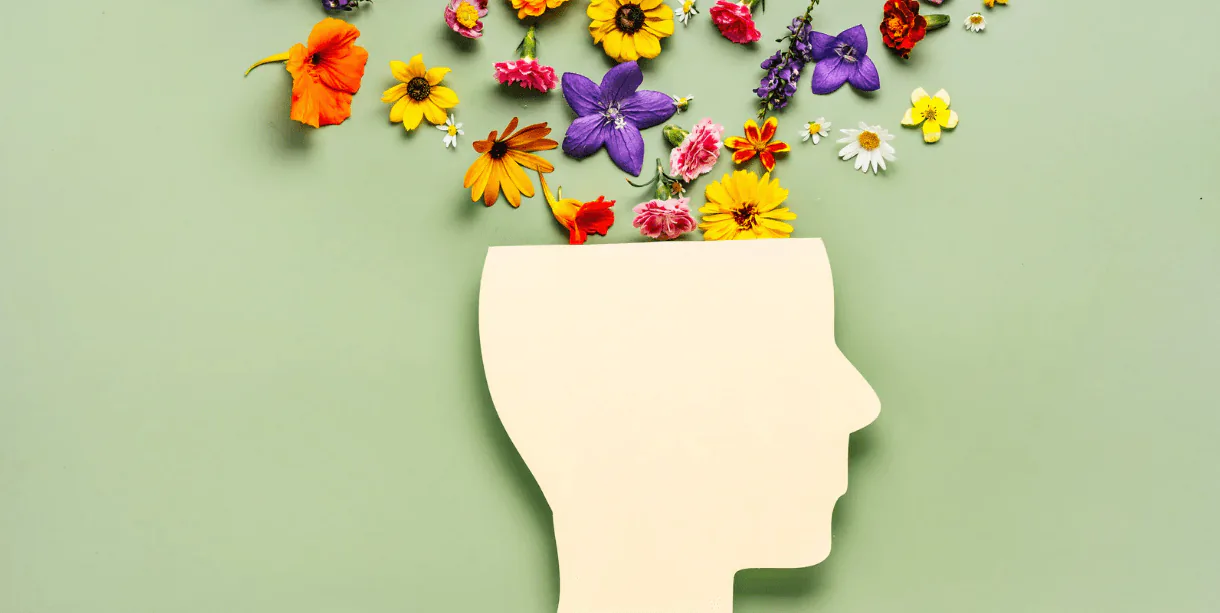 Paper cut-out of a human head with colorful wildflowers spilling from the top on a green background