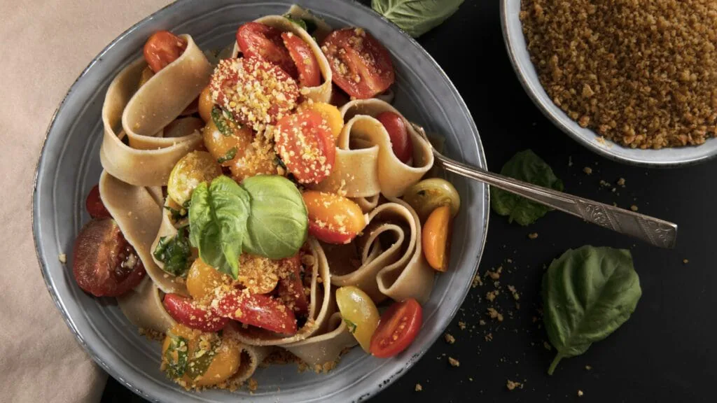 Bowl of wide pasta ribbons tossed with cherry tomatoes, basil and toasted breadcrumbs