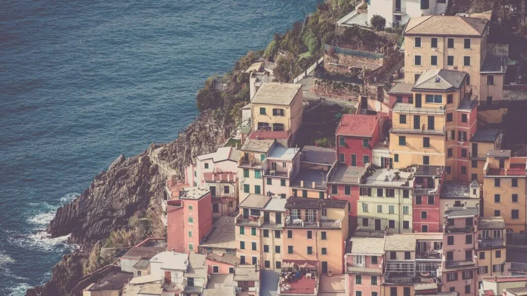 Pastel houses stacked up a cliff above the sea in a Mediterranean coastal village