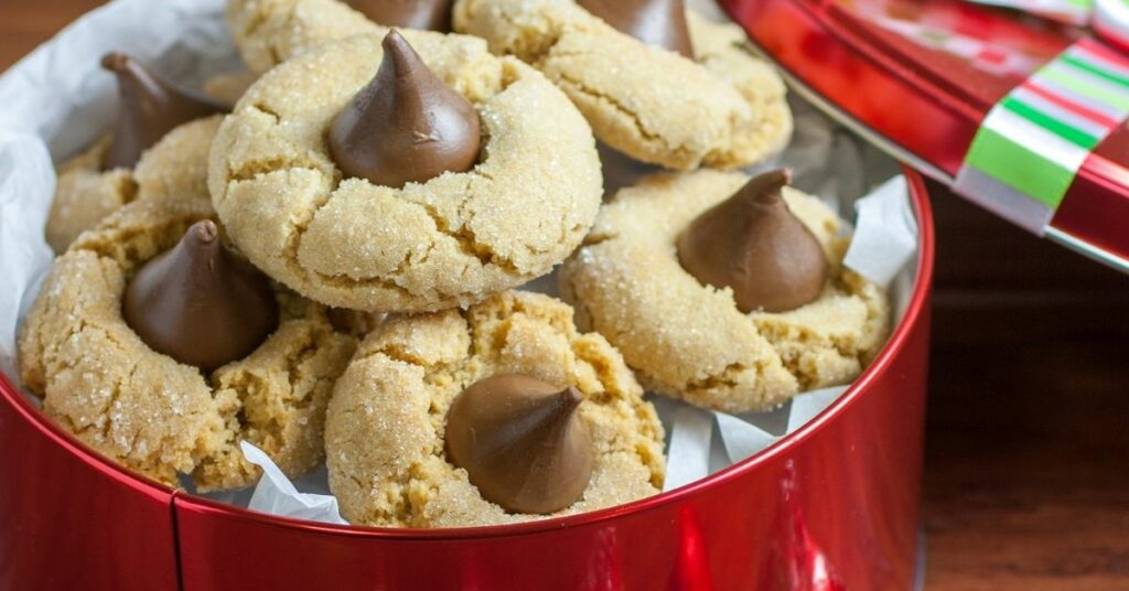 Peanut butter blossom cookies topped with chocolate kisses in a red holiday tin