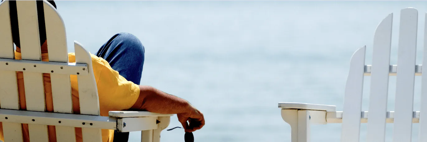 Person resting in a white Adirondack chair looking out over calm open water