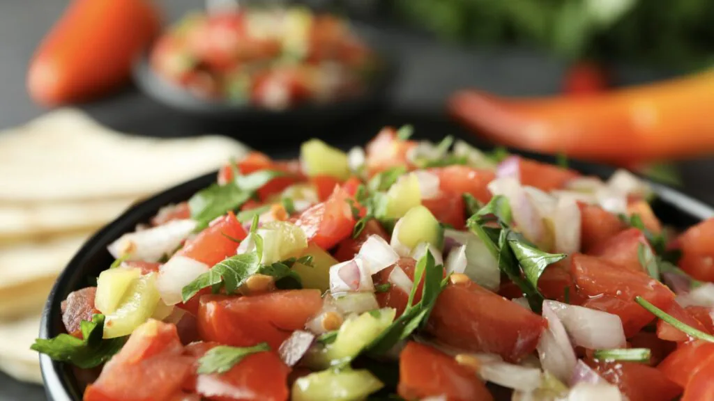 Close-up of fresh pico de gallo with diced tomato, onion and cilantro beside tortilla chips and chilies