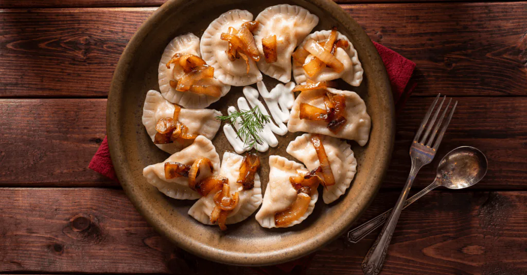 Plate of pierogi dumplings topped with caramelized onions and dill on a rustic wooden table