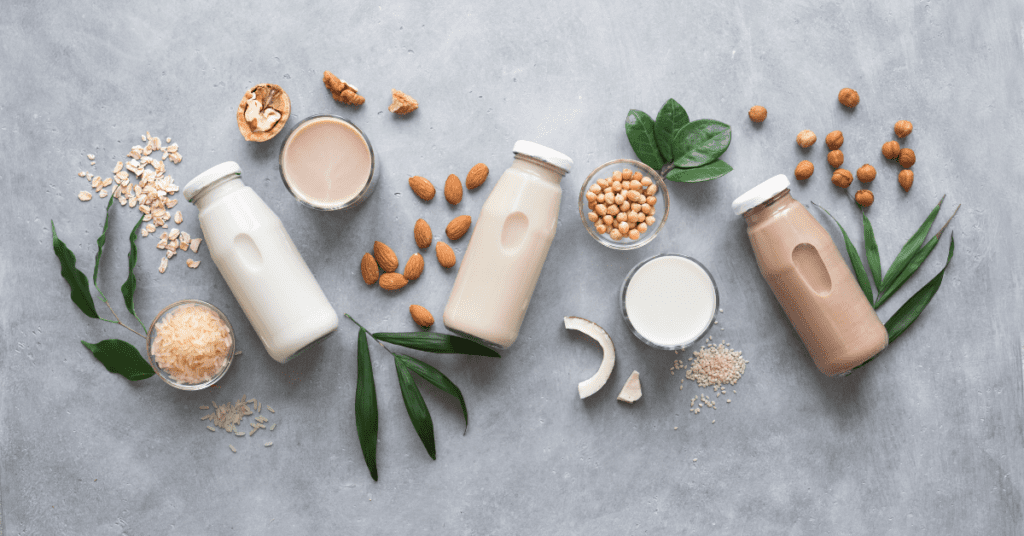 Bottles of plant-based milk surrounded by almonds, oats, soybeans, coconut and sesame seeds