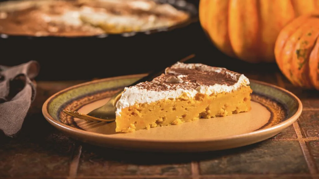 Slice of pumpkin pie topped with whipped cream and cinnamon on a plate with pumpkins behind
