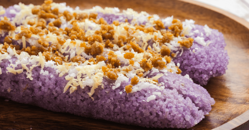Puto bumbong, purple rice cakes topped with grated coconut and brown sugar on a wooden plate