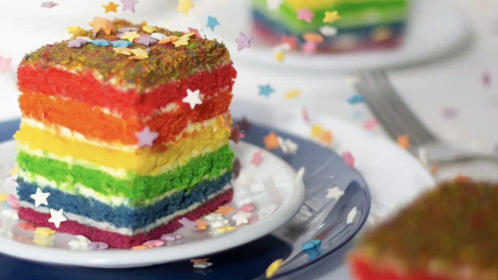 Slice of six-layer rainbow cake covered in star sprinkles on a white plate