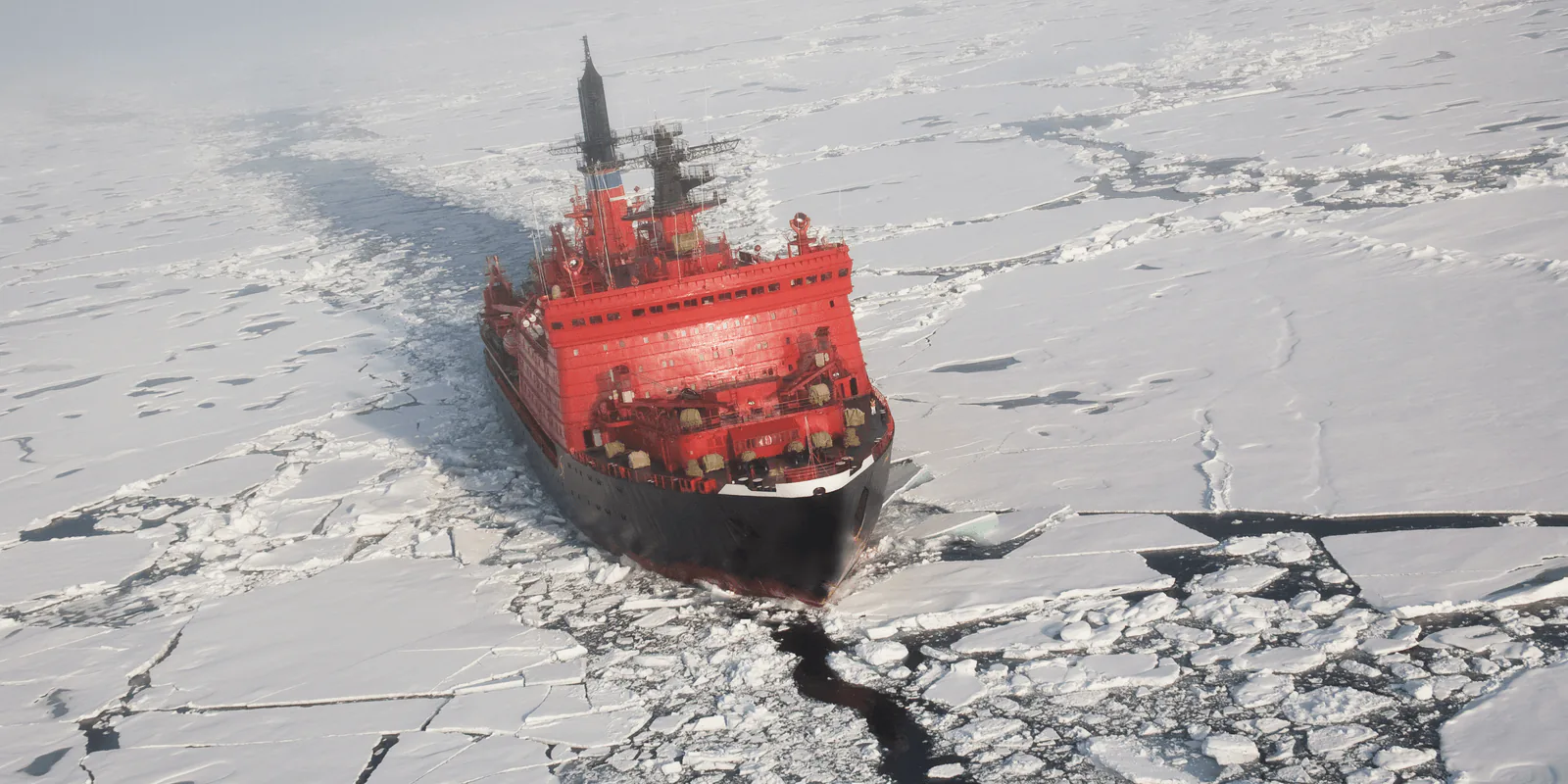Aerial view of a red icebreaker ship cutting a channel through frozen sea ice