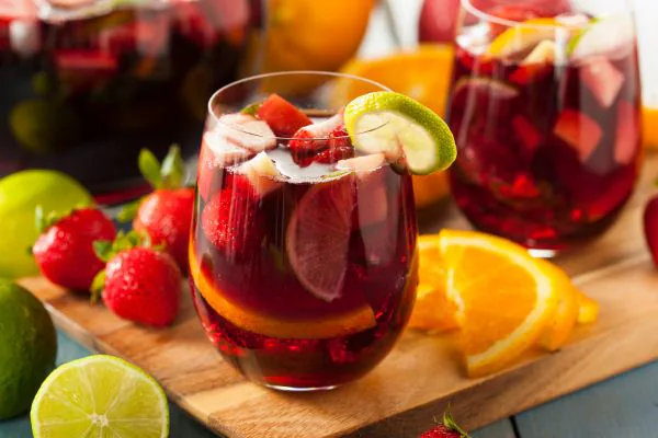 Glasses of red sangria filled with lime, orange slices and raspberries beside fresh fruit