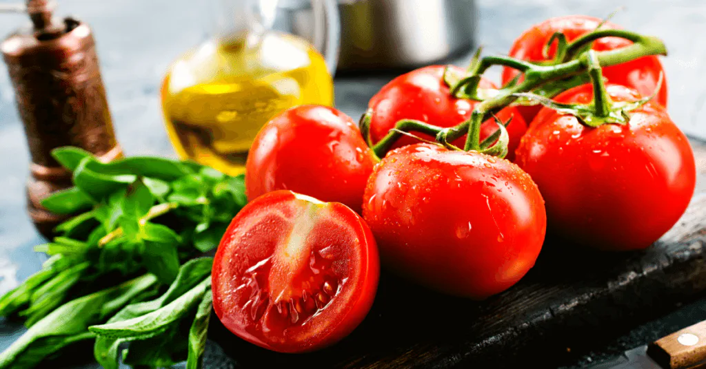 Ripe vine tomatoes, one cut in half, with fresh basil and a bottle of olive oil on a board