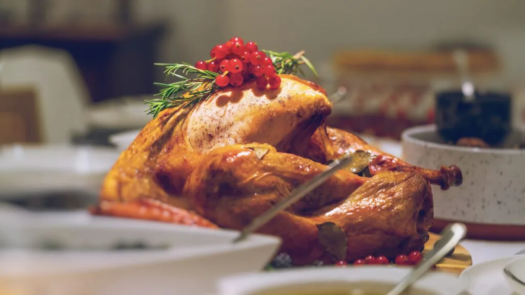 Whole roast turkey garnished with rosemary and red berries on a laid holiday table