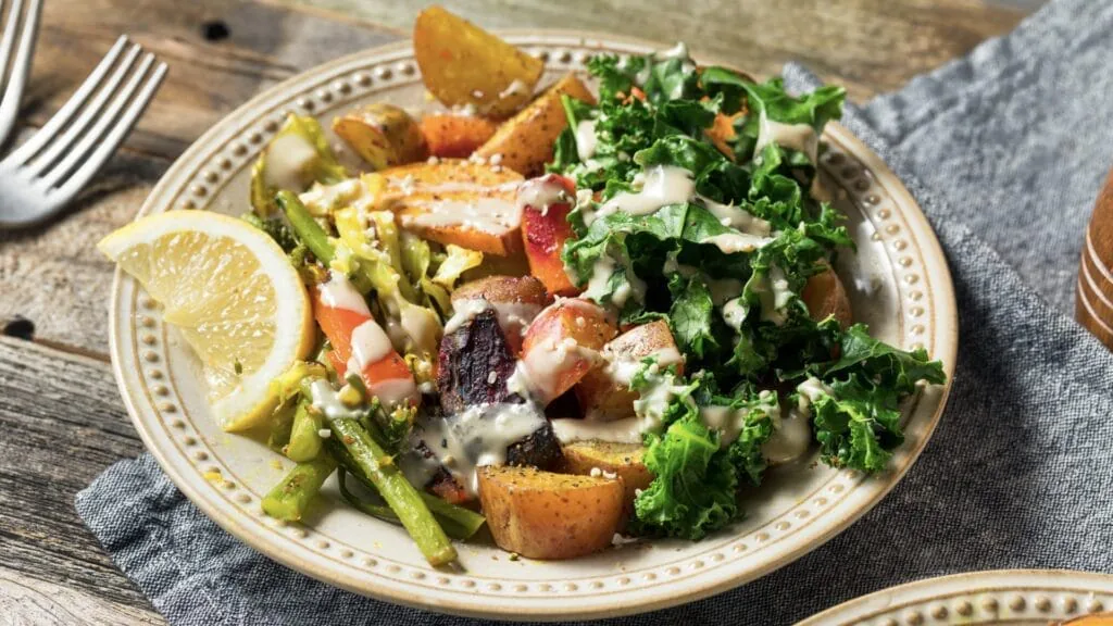 Plate of roasted potatoes, asparagus, beets and kale with creamy dressing and a lemon wedge