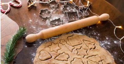 Rolled cookie dough with festive shapes cut out, a rolling pin and metal cookie cutters on a table