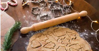 Rolled cookie dough with festive shapes cut out, a rolling pin and metal cookie cutters on a table