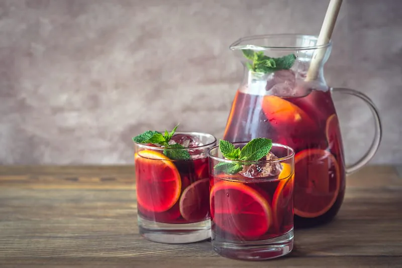 Pitcher of red sangria with orange slices and mint beside two filled glasses