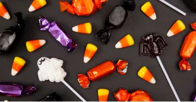 Candy corn, wrapped sweets, lollipops and ghost-shaped gummies scattered on a black surface