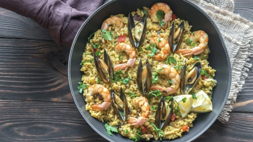 Pan of saffron paella with shrimp, mussels, parsley and a lemon wedge