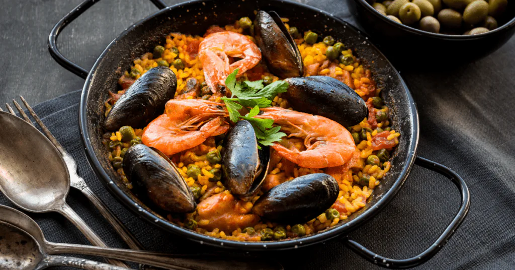 Seafood paella with shrimp, mussels and peas in a black pan, garnished with parsley