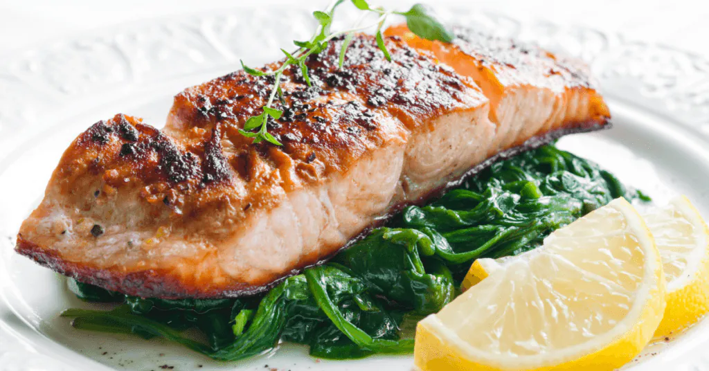 Seared salmon fillet on a bed of wilted spinach with lemon wedges and fresh herbs
