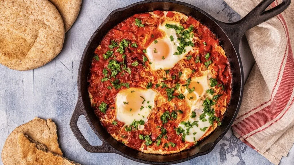 Cast iron skillet of shakshuka with eggs poached in spiced tomato sauce, served with pita bread