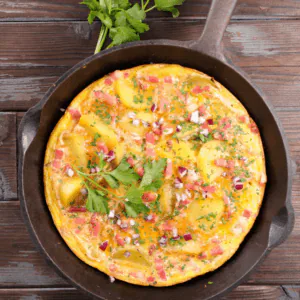 Open-faced omelet with diced ham, potatoes and fresh parsley in a cast-iron skillet