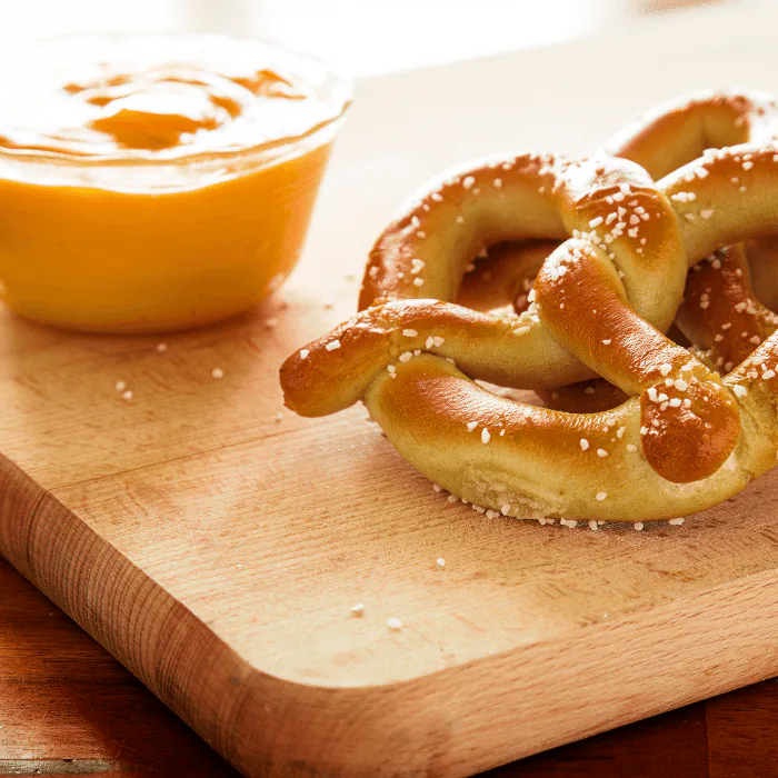 Salted soft pretzel on a wooden board next to a bowl of golden beer cheese dip