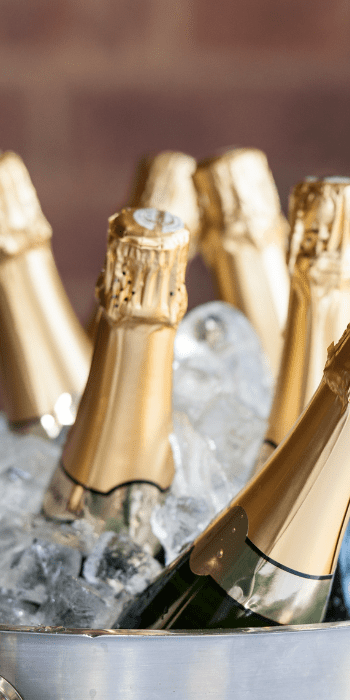 Gold-foiled sparkling wine bottles chilling on ice in a silver bucket