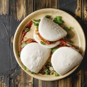 Steamed bao buns filled with crispy cutlet and cilantro on a round plate over rustic wood