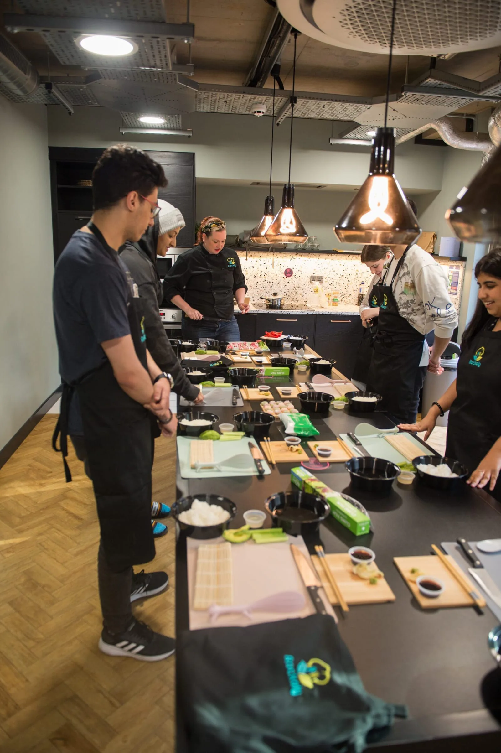 Participants in black aprons at individual sushi rolling stations in a modern kitchen workshop