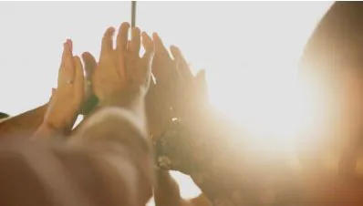 Group of hands meeting in a high five with the sun flaring behind them
