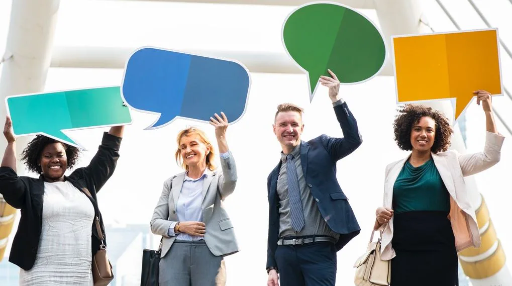Four colleagues in business dress holding colorful speech bubble cutouts above their heads