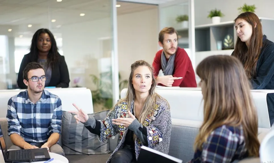 Colleagues talking together on couches in a bright office lounge as one woman gestures