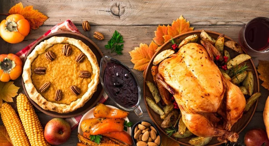 Overhead Thanksgiving table with roast turkey, pumpkin pie, cranberry sauce, corn and persimmons