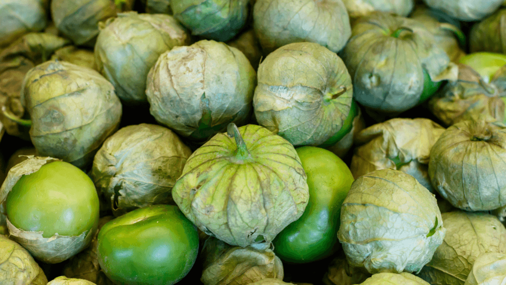 Fresh green tomatillos, some still wrapped in their papery husks, piled together