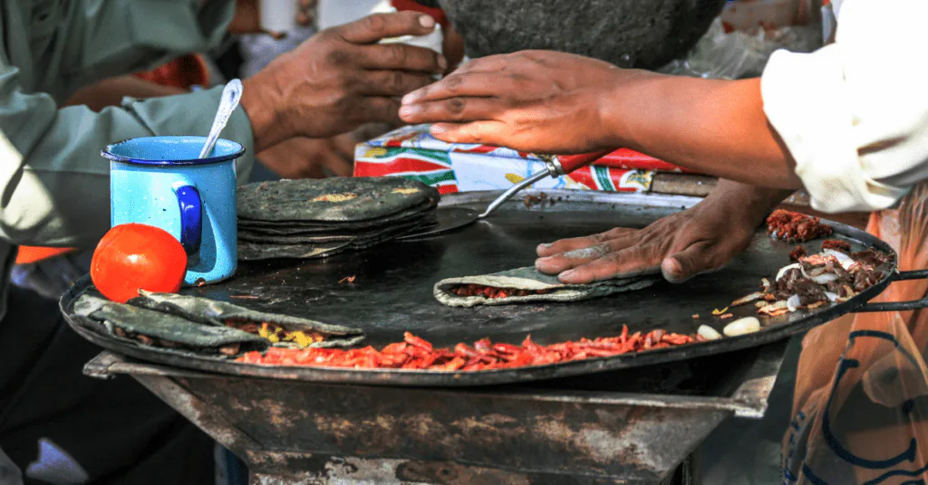 Hands turning tortillas and quesadillas on a hot comal at a Mexican street food stall