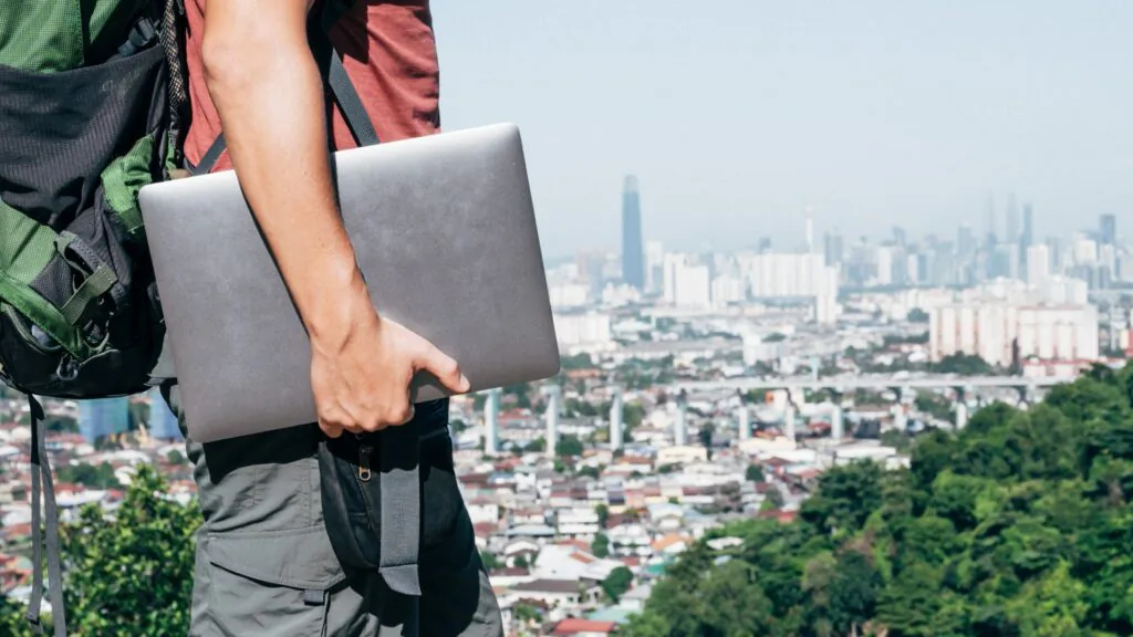 Traveler carrying a backpack and a laptop while overlooking a city skyline