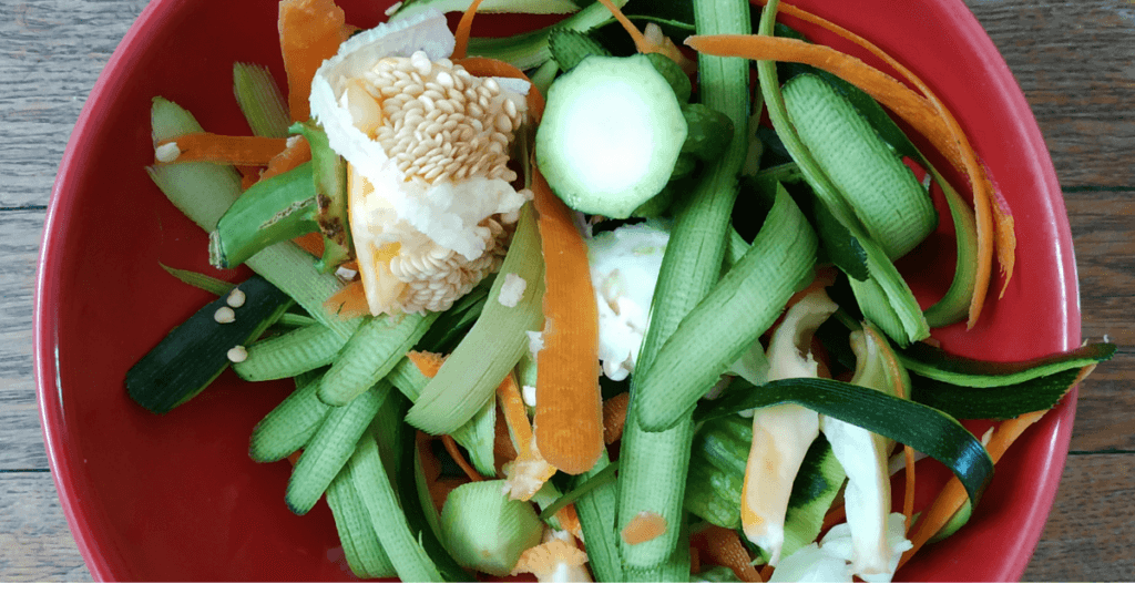 Red bowl filled with cucumber peel, carrot ribbons and other vegetable scraps