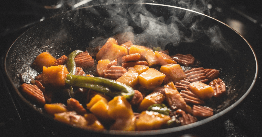 Chunks of vegetables sizzling and steaming in a wide, shallow frying pan