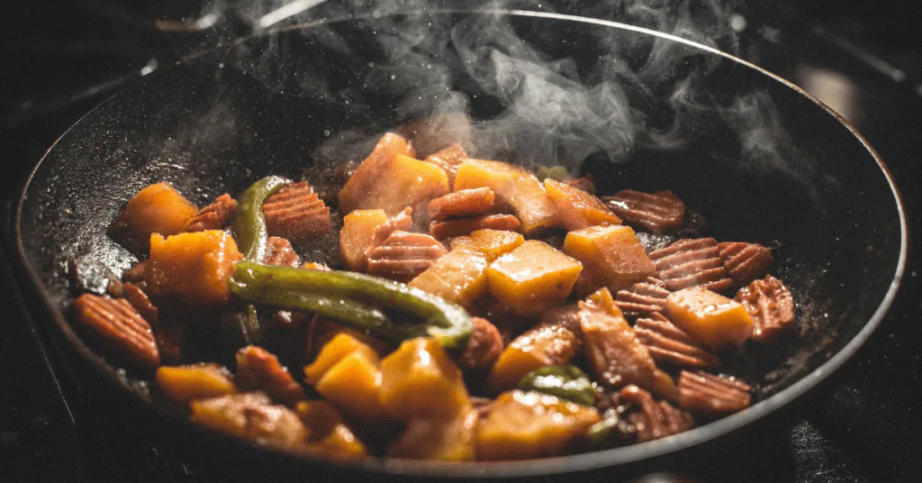 Chunks of vegetables sizzling and steaming in a wide, shallow frying pan