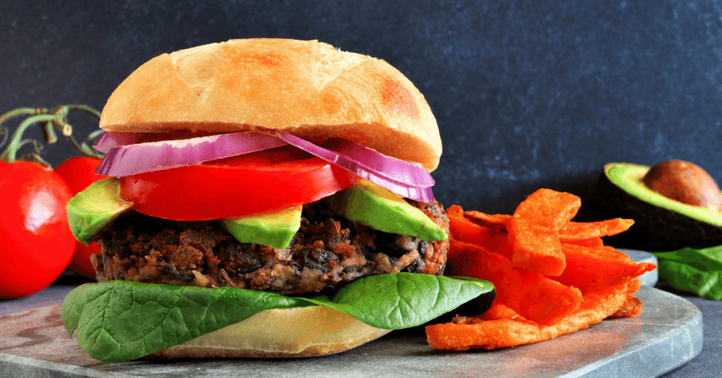 Plant-based burger with avocado, tomato, red onion and spinach beside sweet potato fries