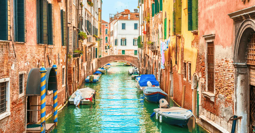 Narrow Venice canal lined with weathered pastel buildings and small boats moored along the walls