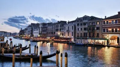 Gondolas moored on Venice's Grand Canal at dusk with lamplit palazzos lining the water
