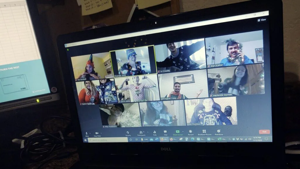 Video call grid of coworkers in party hats and festive sweaters on a desktop monitor