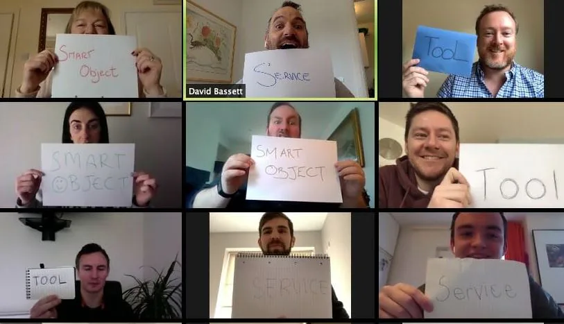 Nine people on a video call holding up handwritten signs reading Smart Object, Service and Tool