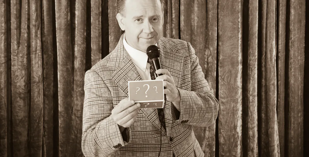 Sepia photo of a vintage game-show host holding a microphone and a card marked with question marks