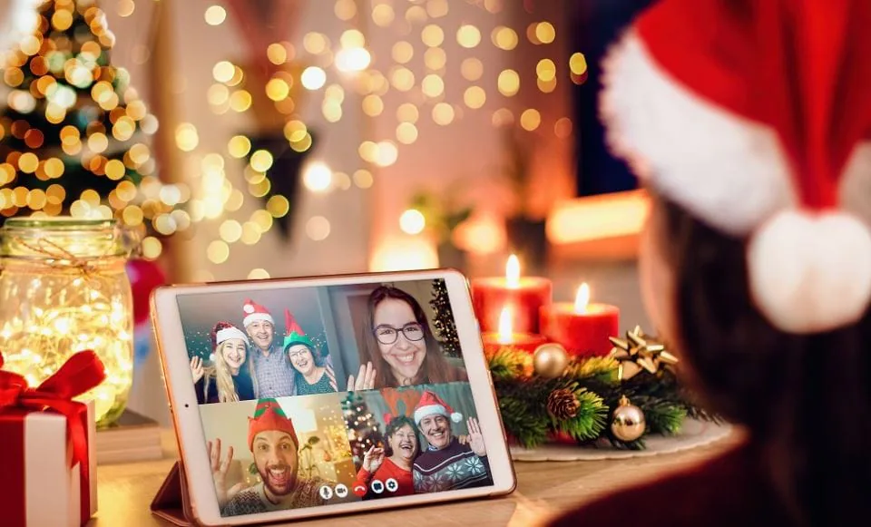 Tablet showing a video call of colleagues in Santa hats waving, beside candles and a Christmas tree