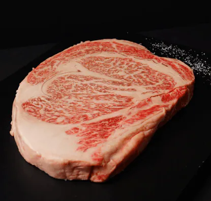 Raw marbled wagyu ribeye steak on a black surface with flakes of sea salt