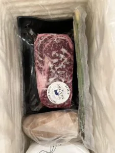 Marbled wagyu steak vacuum-sealed and packed with a cold pack inside a cooking kit shipping box